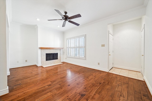 unfurnished living room featuring wood-type flooring, ceiling fan, a tiled fireplace, and crown molding