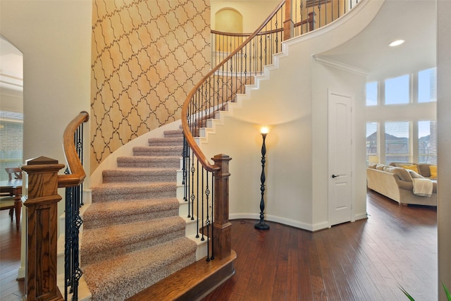 stairs with crown molding, hardwood / wood-style floors, and a towering ceiling