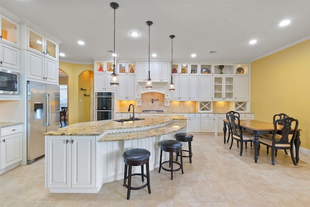 kitchen featuring an island with sink, light stone countertops, sink, appliances with stainless steel finishes, and white cabinets