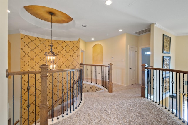 corridor featuring a raised ceiling, an inviting chandelier, crown molding, and carpet floors