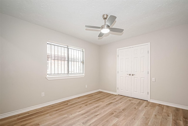 unfurnished bedroom featuring light wood-type flooring, a closet, a textured ceiling, and baseboards