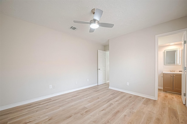 unfurnished bedroom featuring light wood finished floors, baseboards, visible vents, connected bathroom, and a textured ceiling