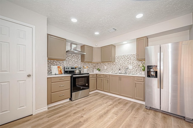 kitchen with stainless steel appliances, light countertops, light wood-style floors, and wall chimney range hood