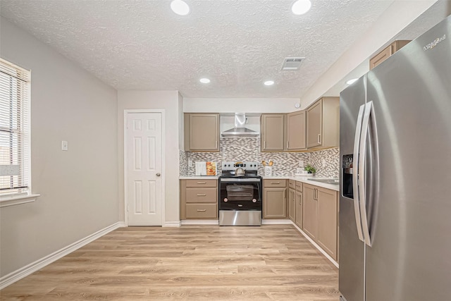 kitchen featuring light countertops, appliances with stainless steel finishes, light wood-type flooring, and wall chimney range hood