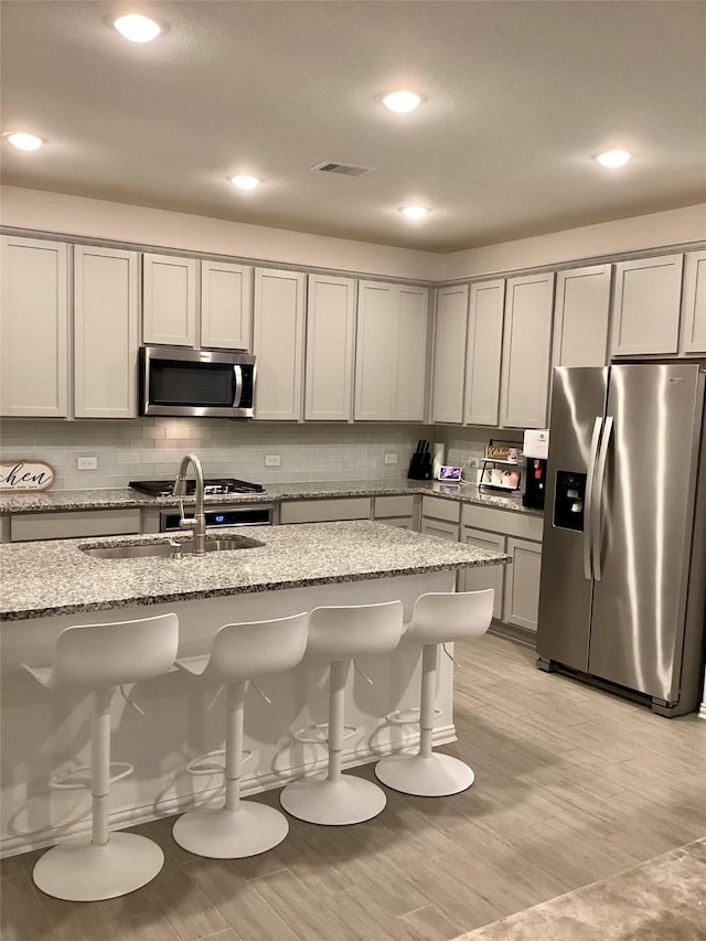 kitchen with sink, appliances with stainless steel finishes, a kitchen bar, and light stone counters