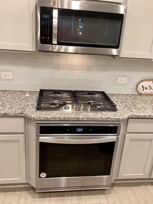 kitchen featuring appliances with stainless steel finishes, decorative backsplash, light stone counters, and white cabinets