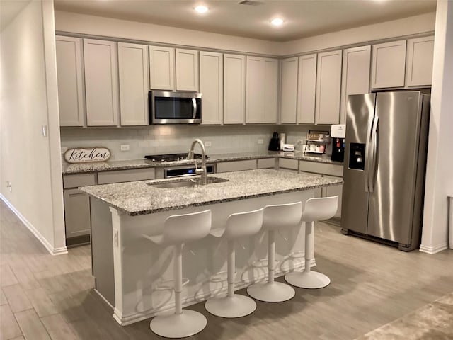 kitchen featuring a breakfast bar, sink, light stone counters, light hardwood / wood-style floors, and stainless steel appliances