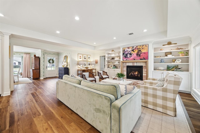 living room with a brick fireplace, built in shelves, and light hardwood / wood-style floors