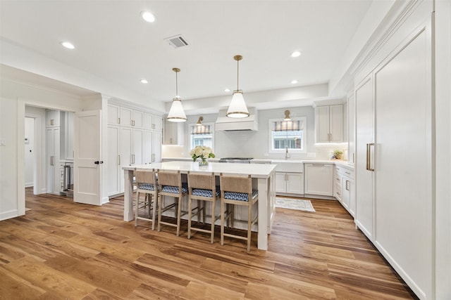 kitchen featuring dishwasher, white cabinets, pendant lighting, a center island, and hardwood / wood-style floors