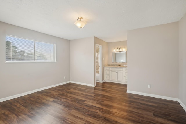unfurnished bedroom featuring dark wood-type flooring, baseboards, and connected bathroom