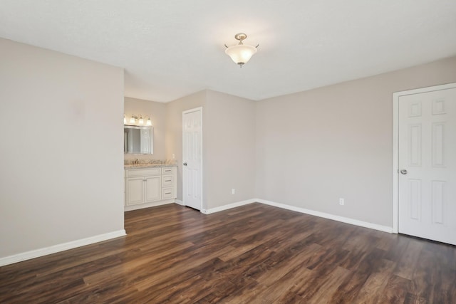 interior space featuring dark wood-type flooring, baseboards, a sink, and connected bathroom