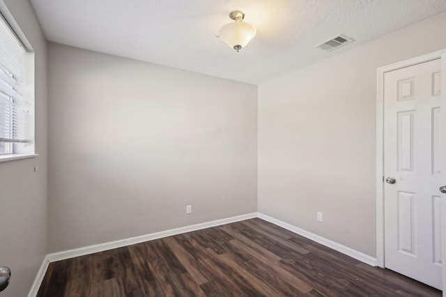 unfurnished room featuring visible vents, baseboards, and dark wood finished floors