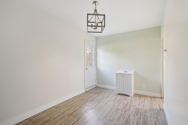 unfurnished dining area with light wood-style flooring, a notable chandelier, and baseboards