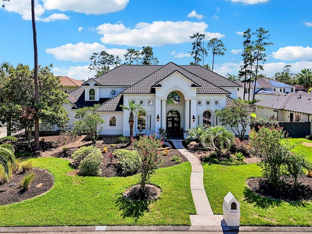 mediterranean / spanish-style home with a residential view, a tiled roof, a front yard, stucco siding, and french doors