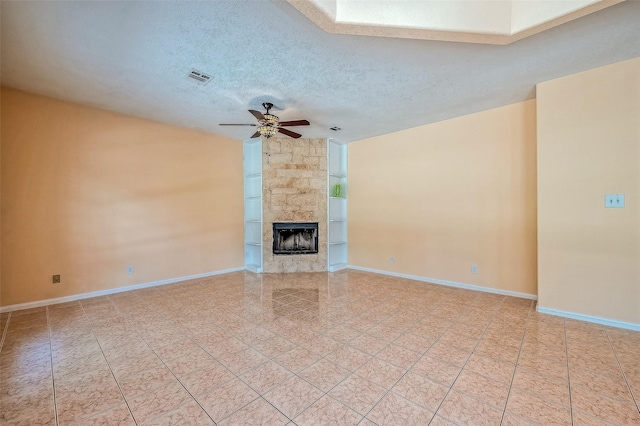 unfurnished living room with light tile patterned flooring, ceiling fan, a large fireplace, and a textured ceiling