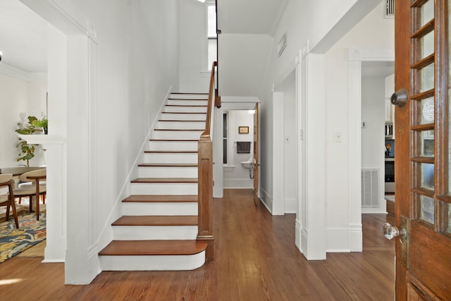 stairway with visible vents, wood finished floors, and ornamental molding