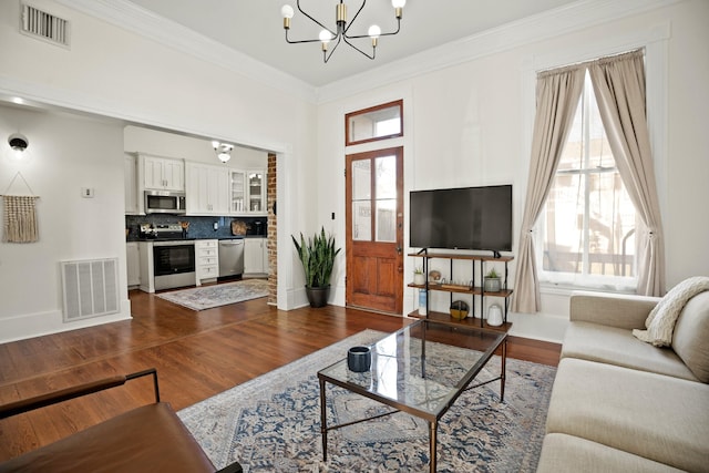 living room featuring dark wood-type flooring, visible vents, a notable chandelier, and ornamental molding