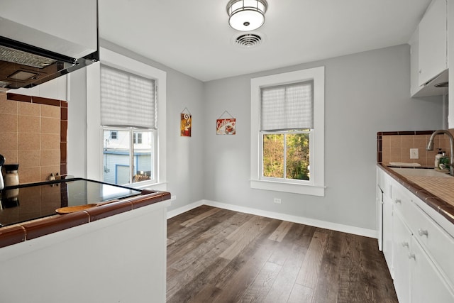 kitchen with dark wood-style flooring, a sink, visible vents, white cabinetry, and decorative backsplash