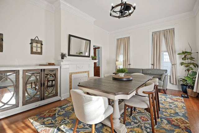 dining area featuring ornamental molding, a tiled fireplace, wood finished floors, and a notable chandelier