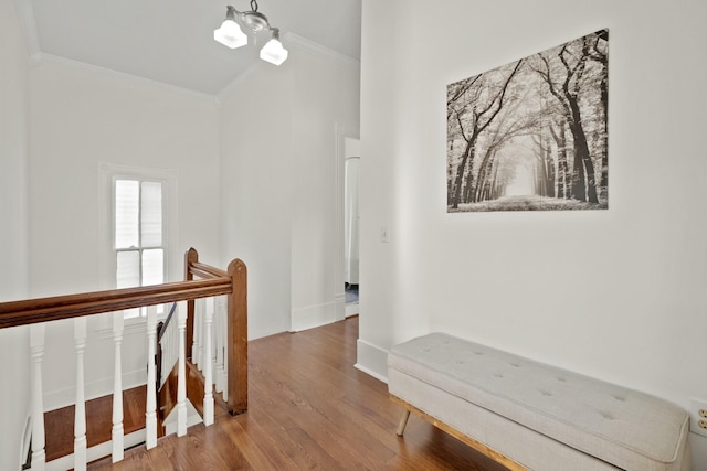 corridor featuring baseboards, ornamental molding, wood finished floors, an upstairs landing, and a chandelier