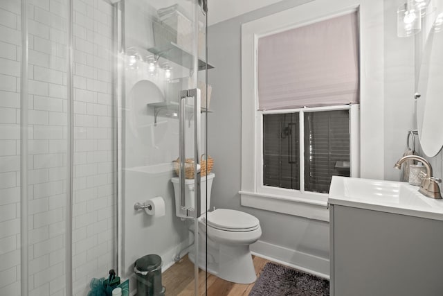 bathroom featuring toilet, wood finished floors, vanity, baseboards, and a tile shower