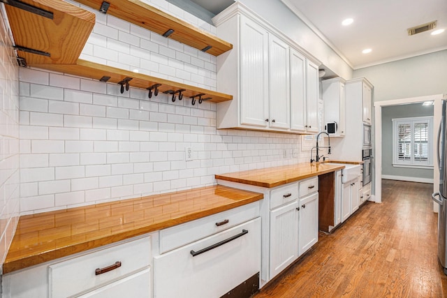 kitchen with white cabinets, appliances with stainless steel finishes, butcher block counters, and tasteful backsplash