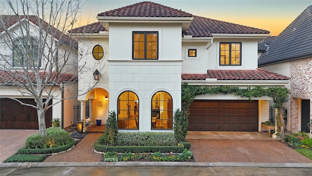 mediterranean / spanish-style house featuring decorative driveway, stucco siding, an attached garage, and a tile roof