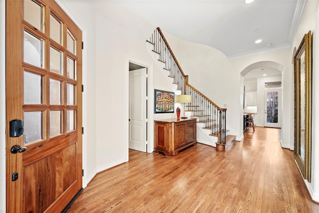 foyer entrance with arched walkways, light wood-style flooring, stairs, and baseboards