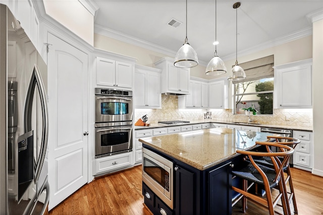 kitchen with light wood finished floors, a kitchen island, crown molding, white cabinets, and stainless steel appliances