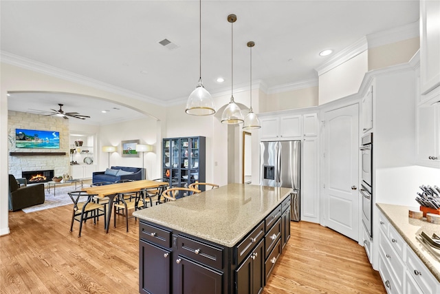 kitchen with visible vents, light wood-style flooring, arched walkways, stainless steel refrigerator with ice dispenser, and white cabinetry