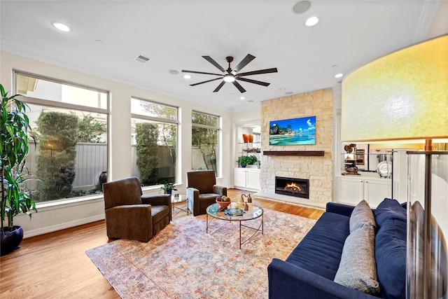 living area with a stone fireplace, recessed lighting, wood finished floors, and ornamental molding