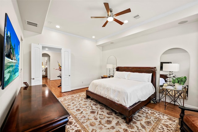 bedroom with wood finished floors, crown molding, visible vents, and arched walkways