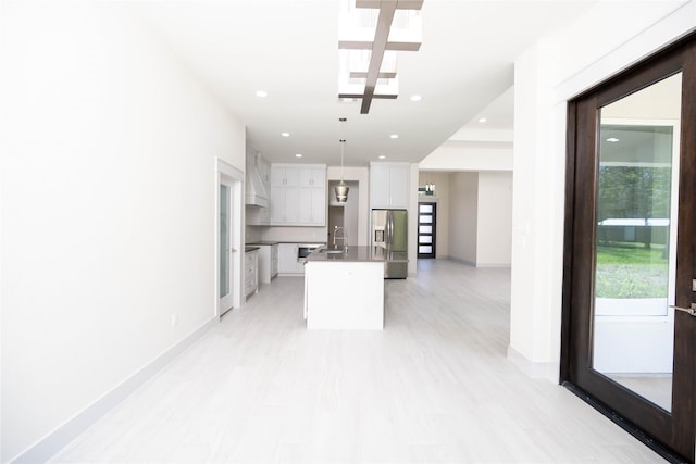 kitchen featuring a center island with sink, white cabinets, stainless steel refrigerator with ice dispenser, pendant lighting, and sink