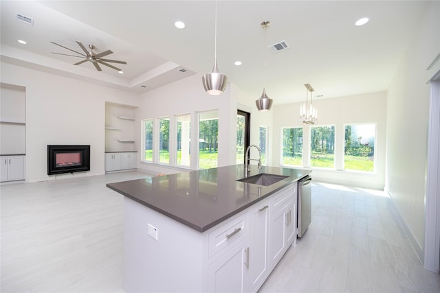 kitchen with white cabinets, stainless steel dishwasher, decorative light fixtures, sink, and a kitchen island with sink