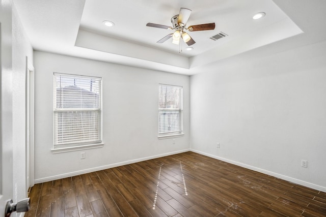 unfurnished room with a tray ceiling, a wealth of natural light, ceiling fan, and dark hardwood / wood-style flooring