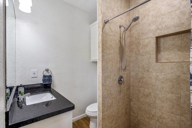 bathroom with toilet, vanity, a tile shower, and wood-type flooring