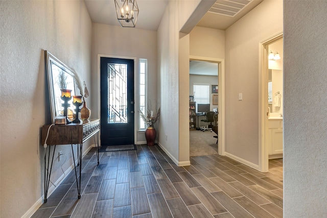 foyer featuring wood finish floors, visible vents, a notable chandelier, and baseboards