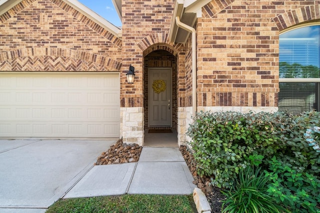 entrance to property with a garage, concrete driveway, brick siding, and stone siding