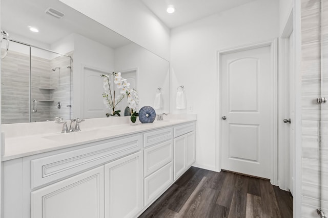 bathroom featuring visible vents, a sink, tiled shower, and wood finished floors