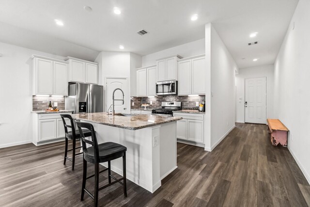 kitchen with a kitchen island with sink, stainless steel appliances, a breakfast bar, a sink, and visible vents