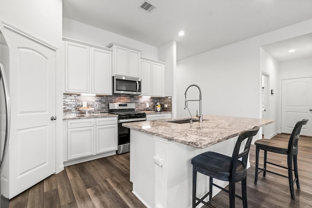 kitchen featuring light stone counters, a center island with sink, backsplash, appliances with stainless steel finishes, and a sink