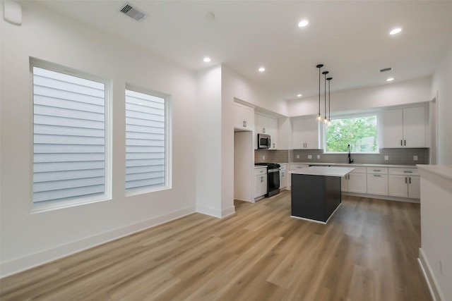 kitchen featuring decorative light fixtures, stainless steel appliances, light countertops, white cabinetry, and a kitchen island