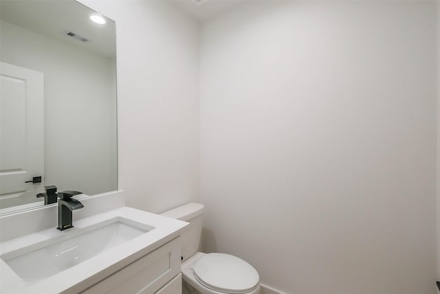 half bathroom with toilet, vanity, and visible vents