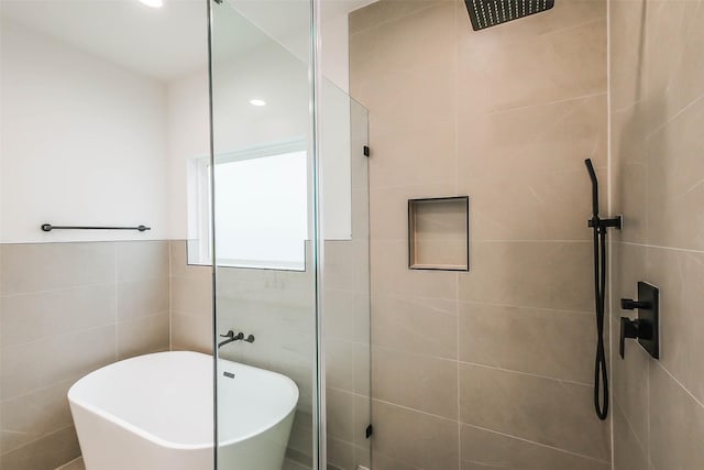 bathroom featuring a walk in shower, a soaking tub, and tile walls