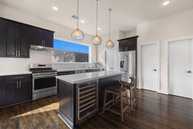 kitchen with wine cooler, stainless steel appliances, light countertops, backsplash, and under cabinet range hood