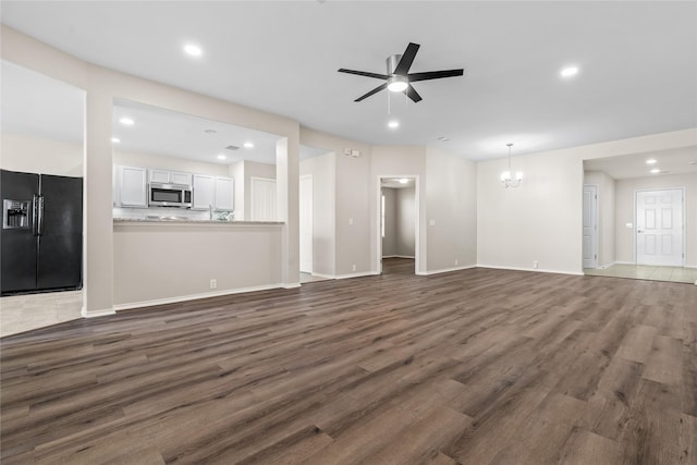 unfurnished living room featuring ceiling fan with notable chandelier, baseboards, dark wood finished floors, and recessed lighting