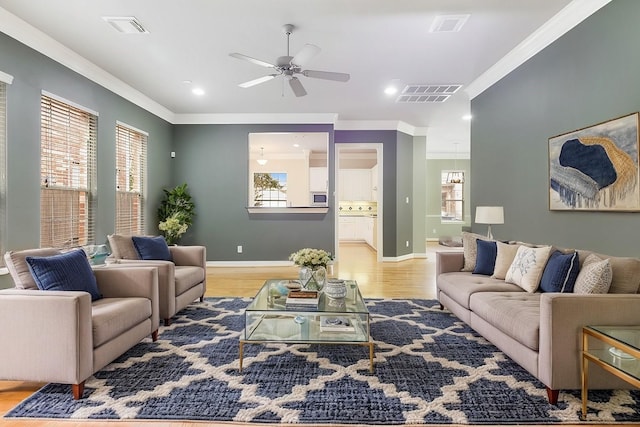 living room featuring light wood-style flooring, visible vents, baseboards, and ornamental molding