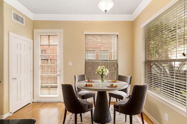 dining space with light wood-style floors, baseboards, visible vents, and crown molding