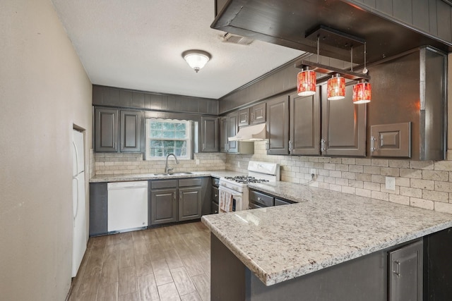 kitchen with white appliances, a sink, under cabinet range hood, a textured ceiling, and tasteful backsplash