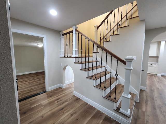 staircase featuring arched walkways, wood finished floors, and baseboards